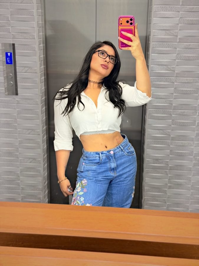 Anita Bikava con blusa blanca y jean, foto en espejo